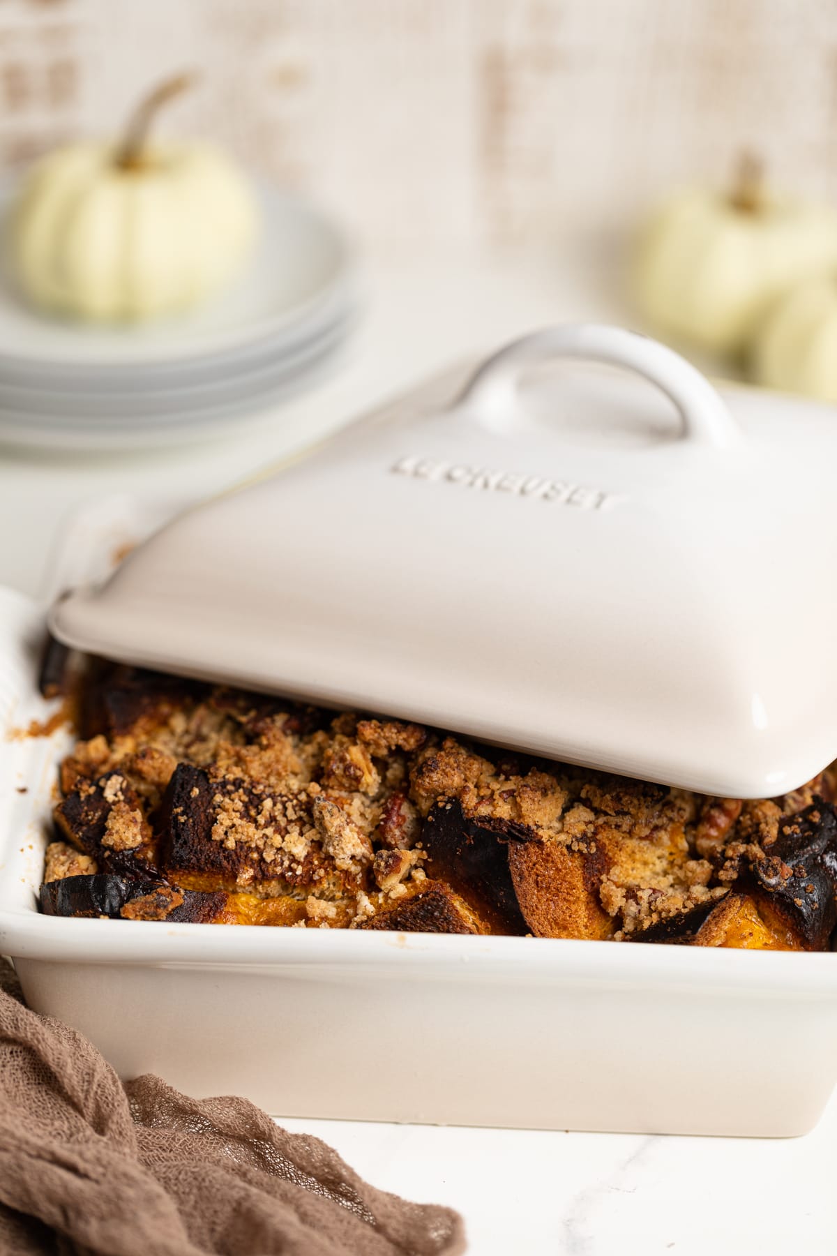 Baked Pumpkin French Toast Casserole in a white Le Creuset baking pan with the lid half on