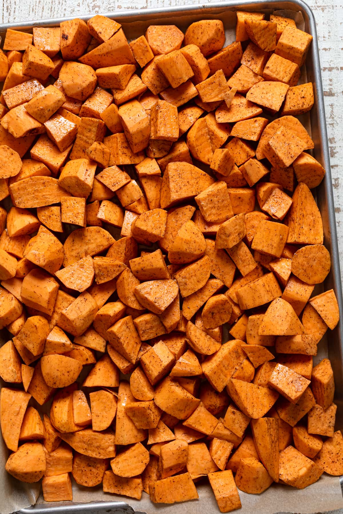 Seasoned, chopped sweet potatoes on a baking sheet