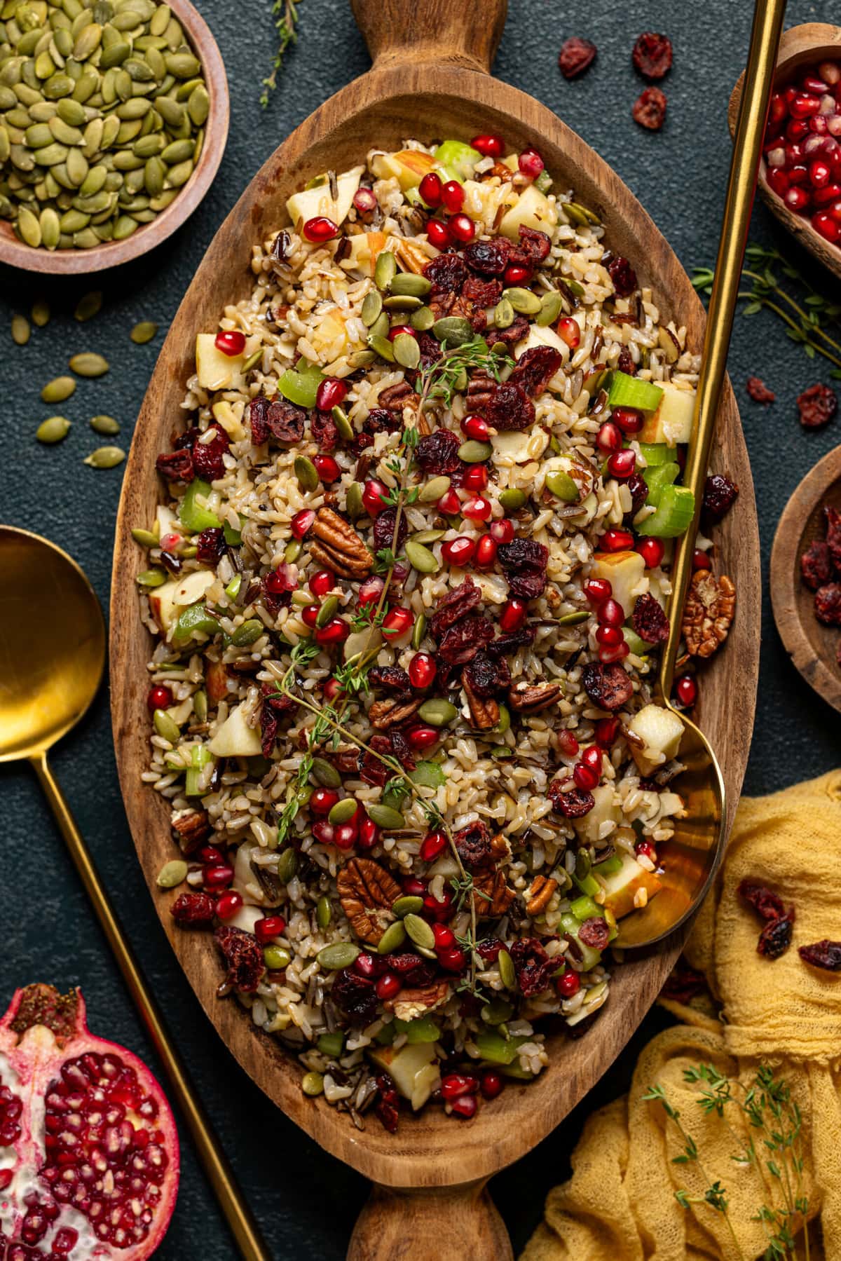 Wild rice in a serving bowl with two gold serving spoons and bowls of ingredients around.