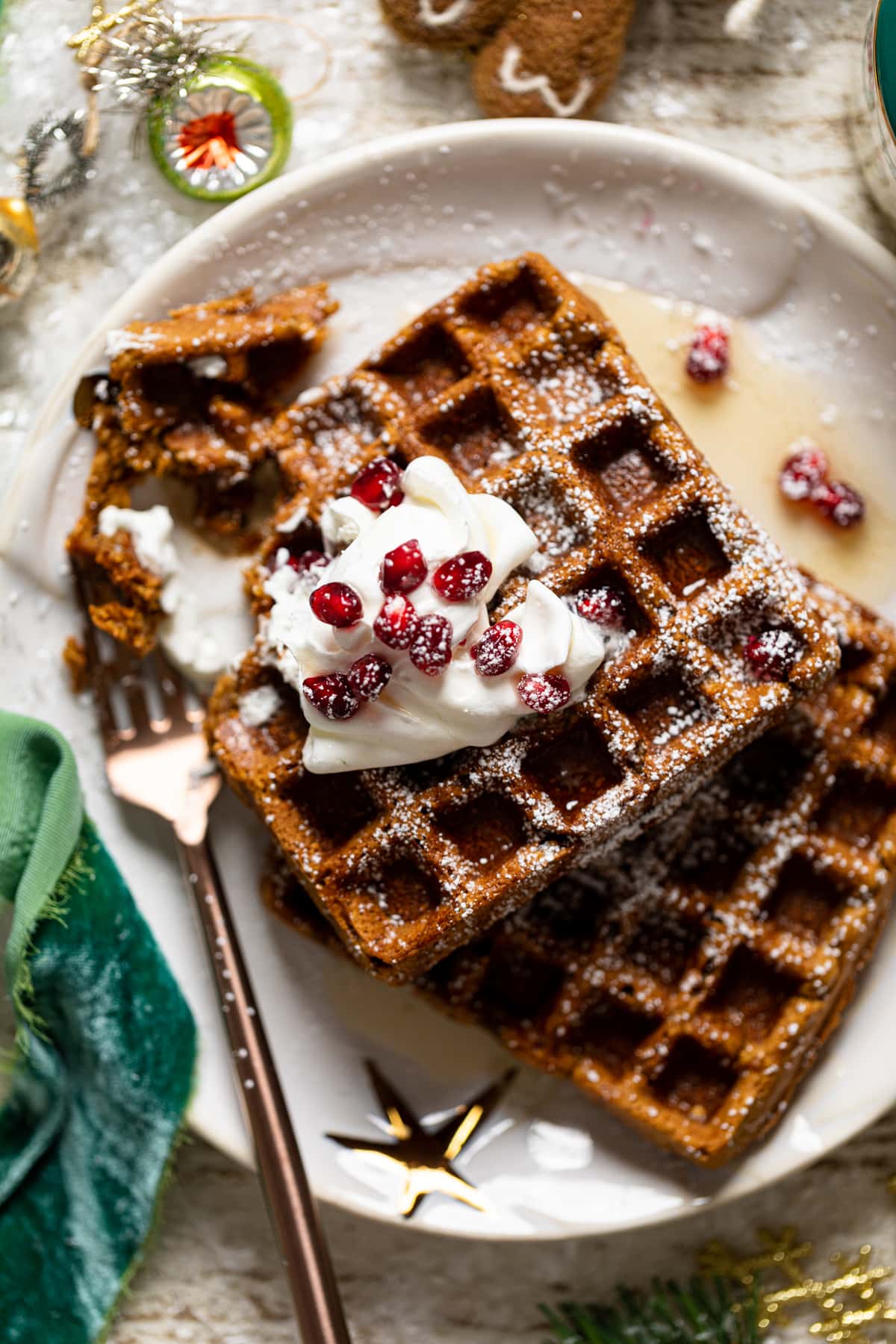 Gluten-free Flourless Gingerbread Waffles topped with whipped cream, pomegranate arils, and powdered sugar.