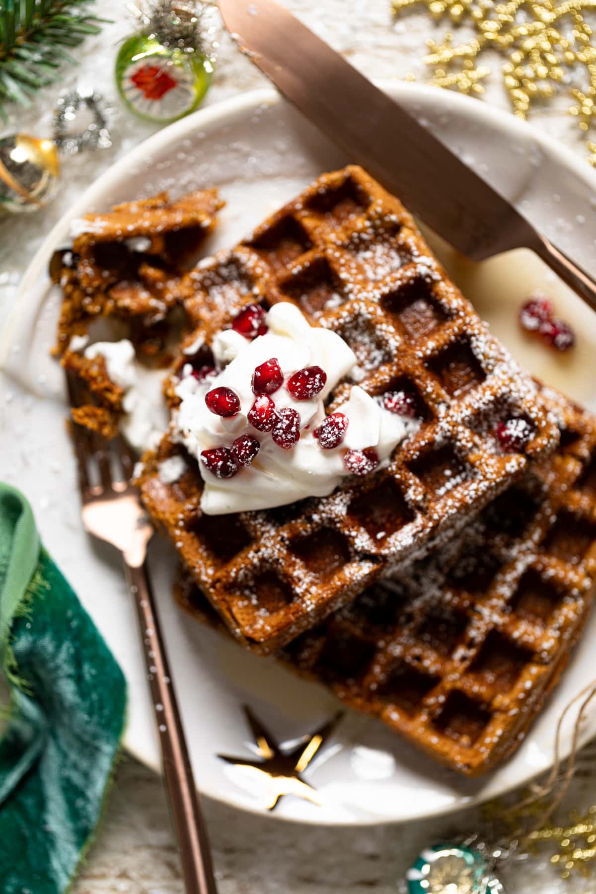 Gluten-free Flourless Gingerbread Waffles topped with whipped cream, pomegranate arils, and powdered sugar.