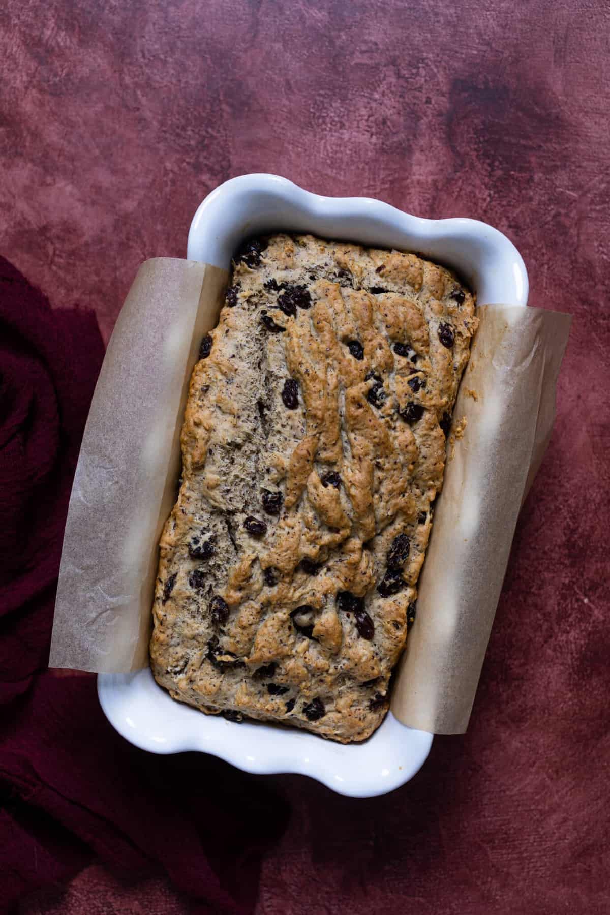 Homemade Rum Raisin Bread in a white baking dish with parchment paper on the sides.