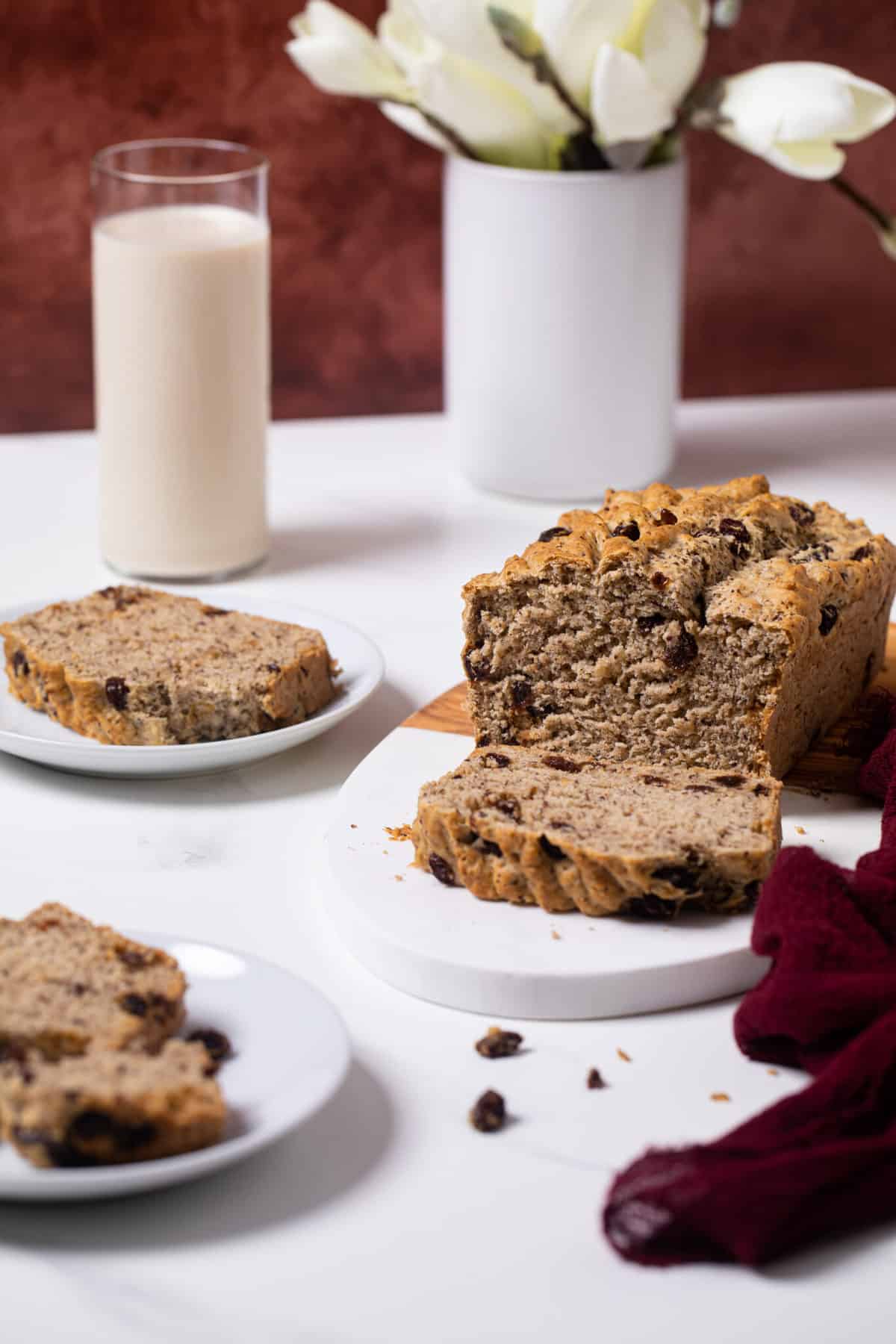 Homemade Rum and Raisin Bread on white plates and the loaf on a cutting board with white flowers in the background.