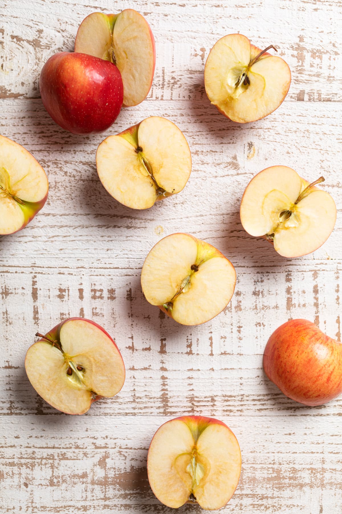 Halved apples on a white, wooden table.