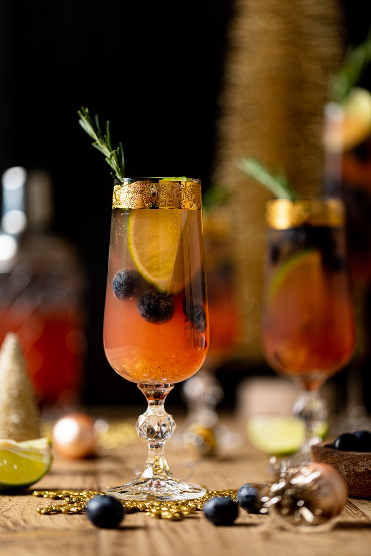 Blueberry Ginger Lime Mocktail topped with a sprig of rosemary in a gold-rimmed, stemmed glass