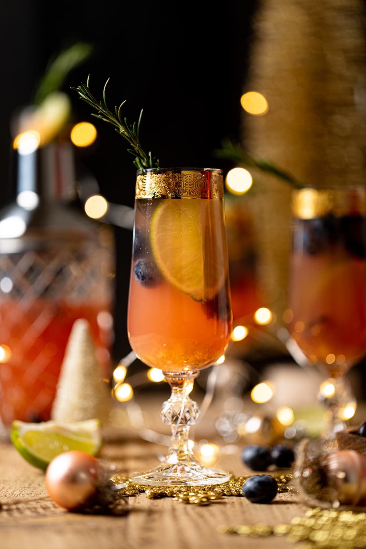 Blueberry Ginger Lime Mocktail topped with a sprig of rosemary in a gold-rimmed, stemmed glass