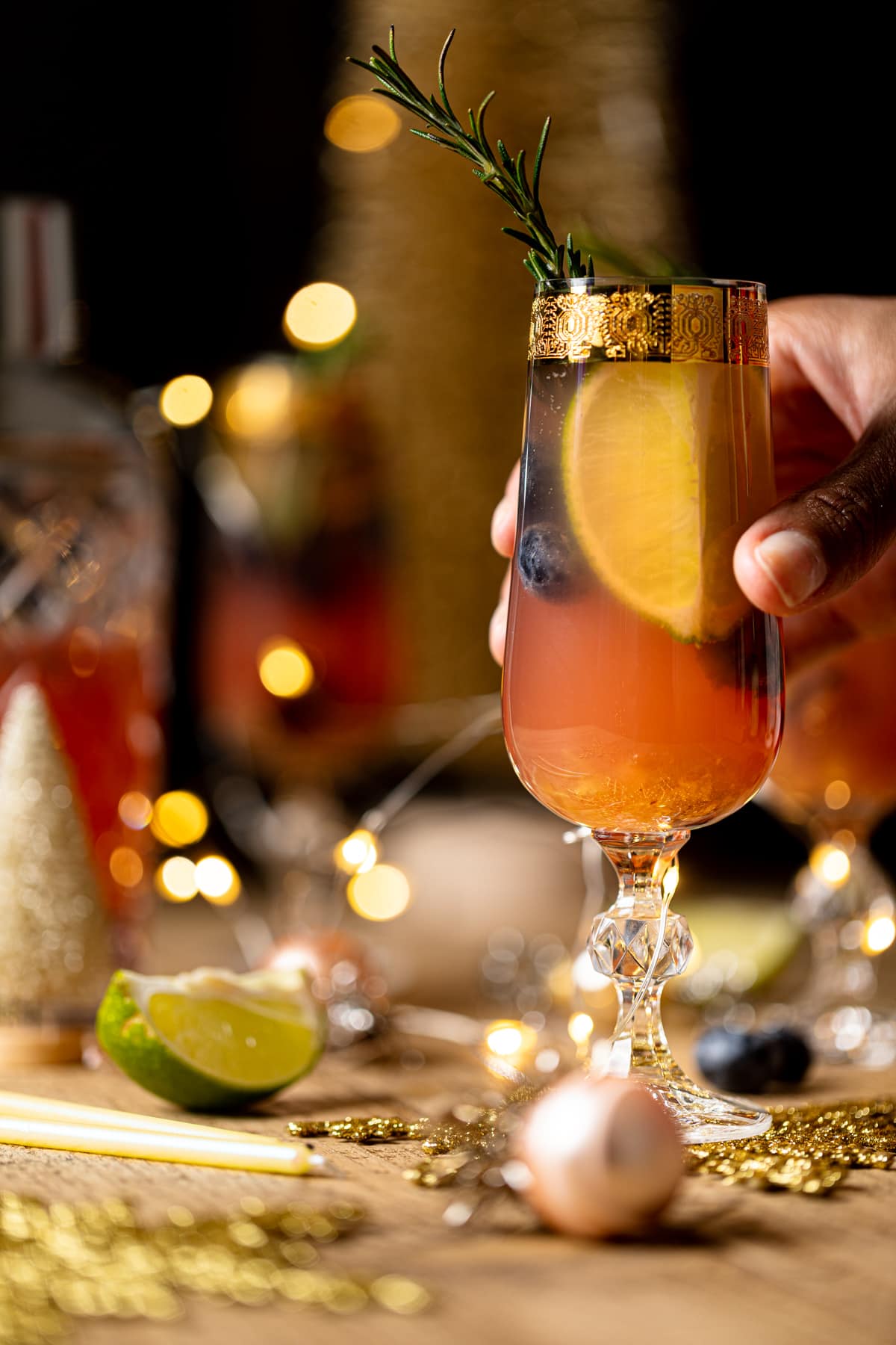 Hand grabbing a Blueberry Ginger Lime Mocktail in a gold-rimmed, stemmed glass