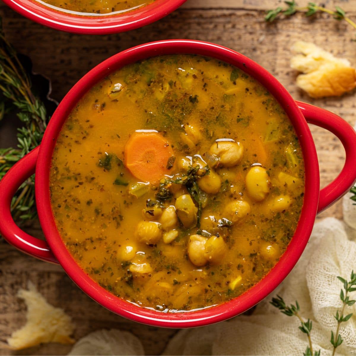 Two red bowls with soup and side of bread on a brown wood table.