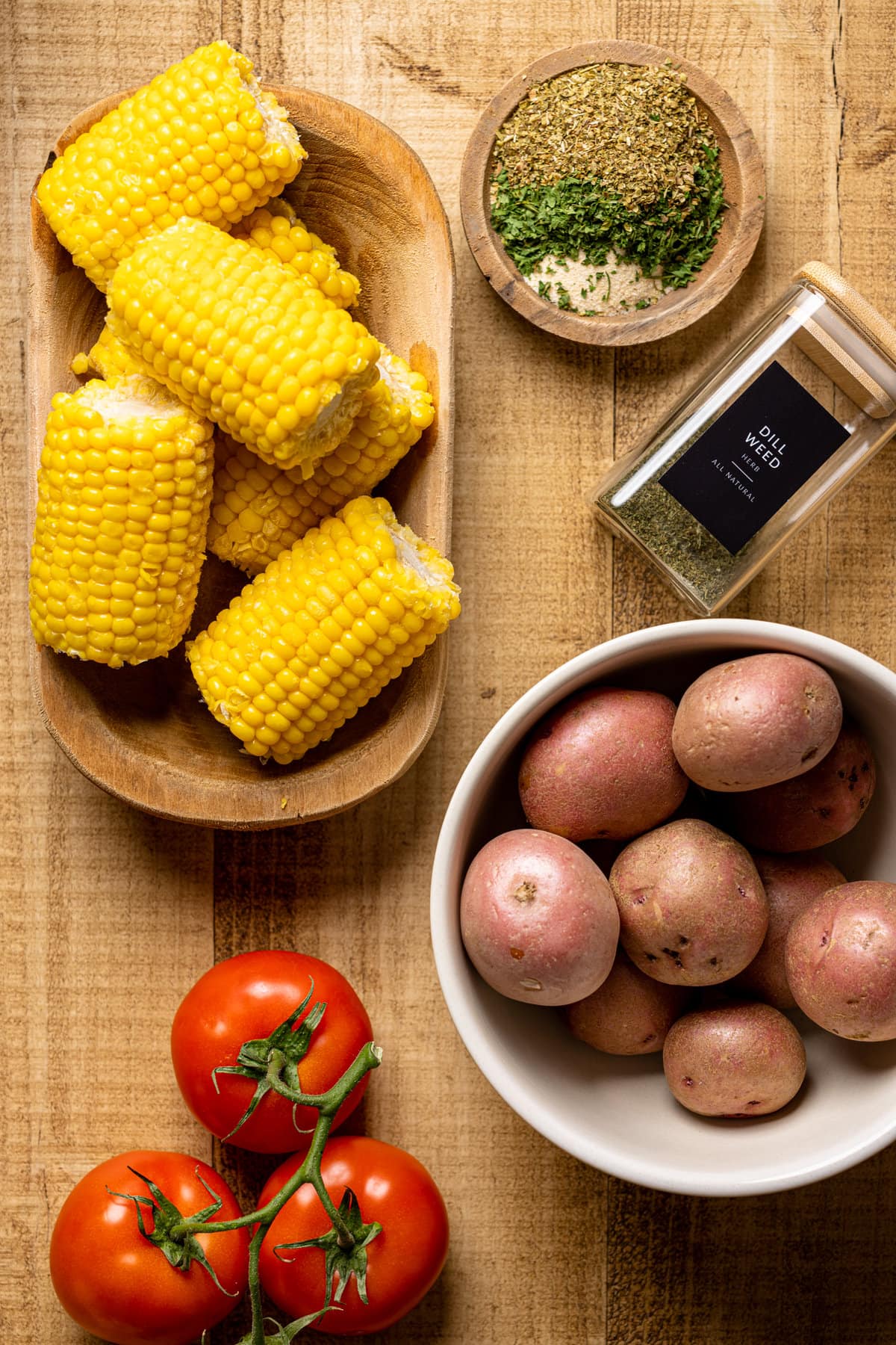 Ingredients for Sheet Pan Garlic Herb Salmon, Lobster, and Veggies including potatoes, corn, and dill weed