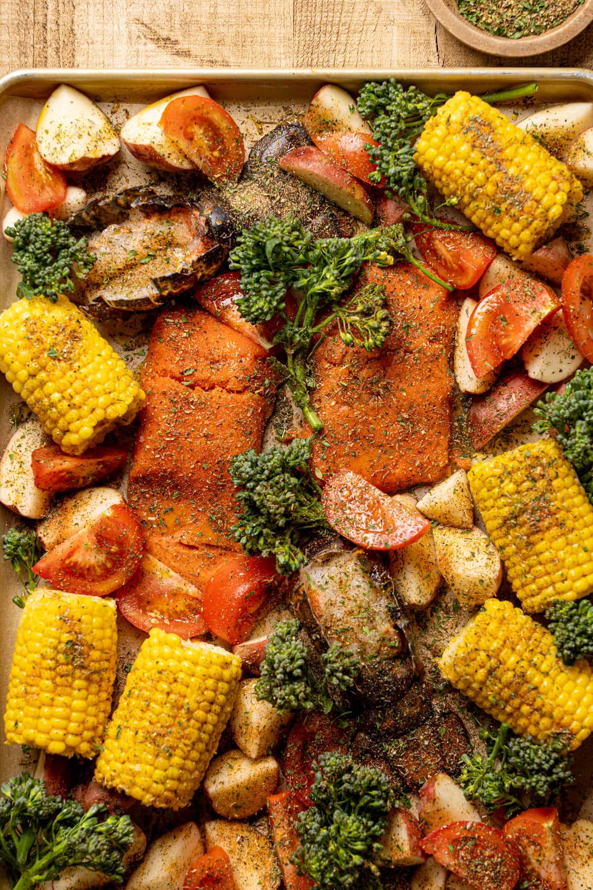 Sheet pan with seasoned and uncooked salmon, lobster, and vegetables 