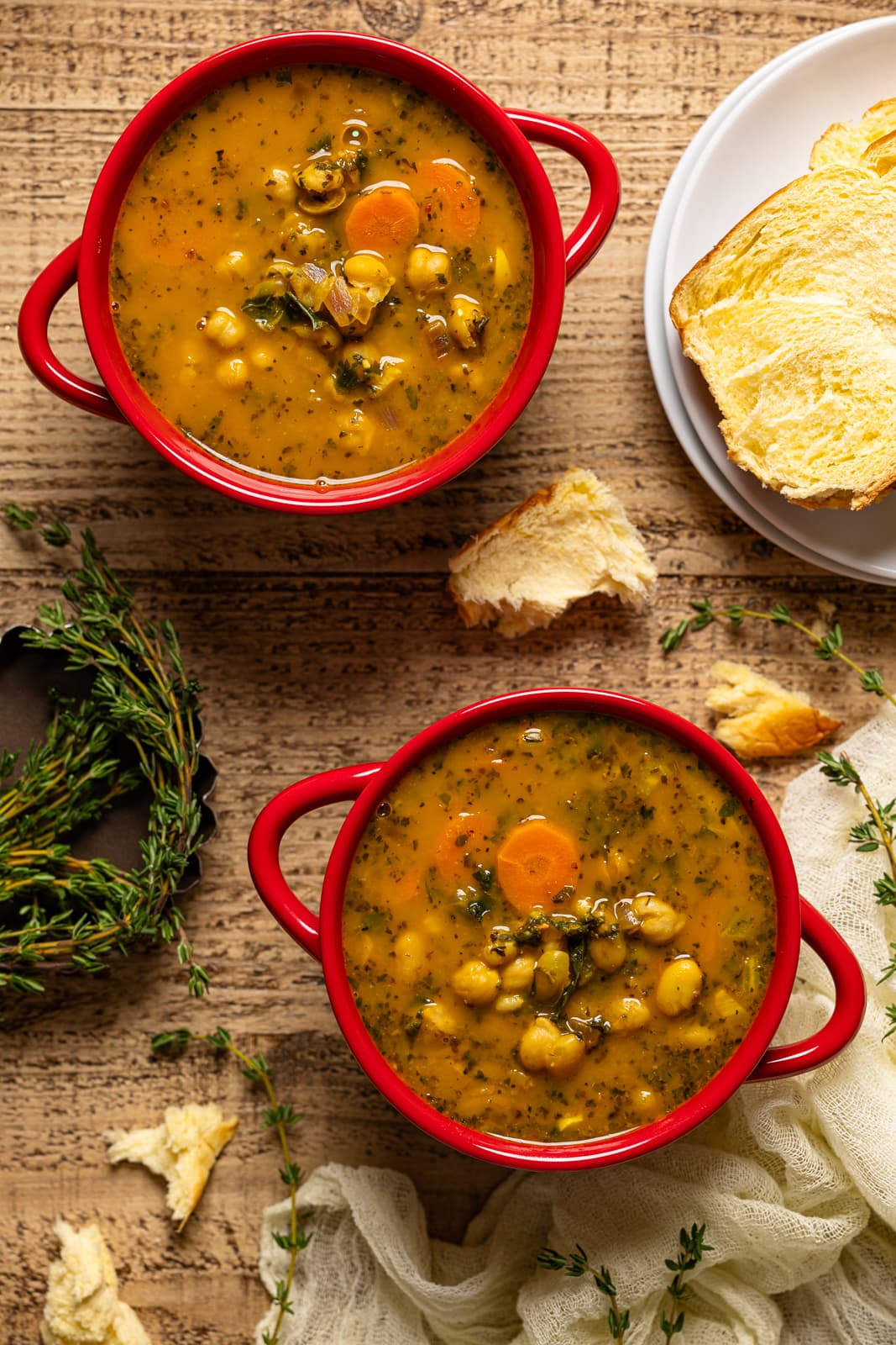 Two red bowls with soup with a plate with bread.