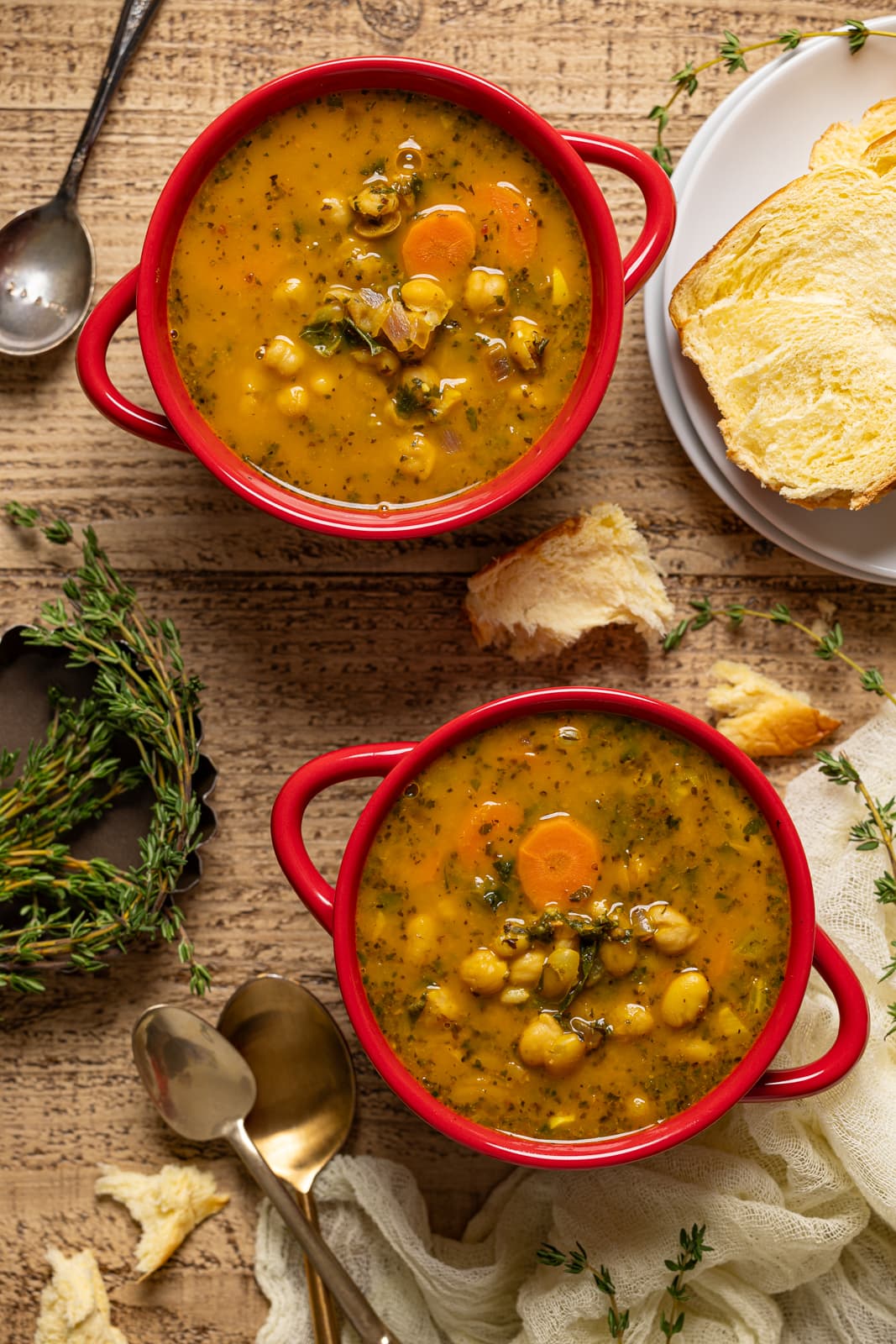 Two red bowls of soup with a side of bread and spoons.