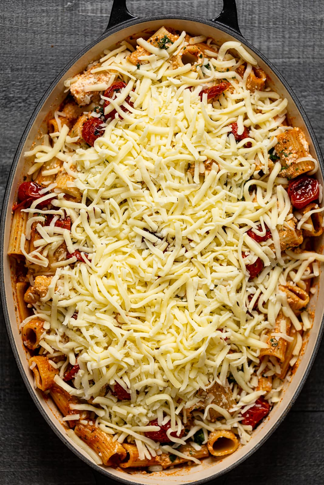 Dutch oven full of ingredients for Meatless Baked Ziti topped with shredded cheese