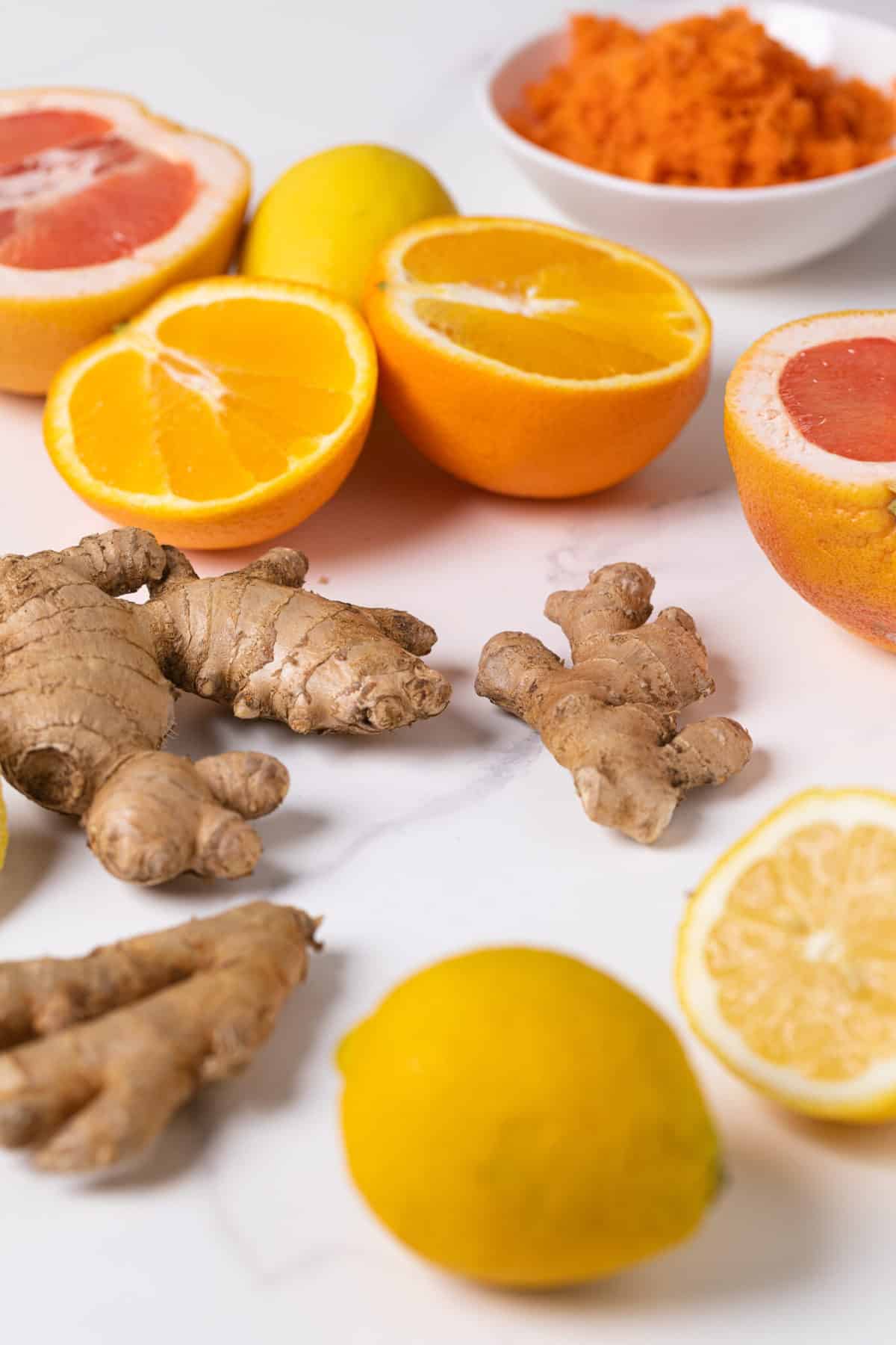 Fresh produce like ginger and oranges on a marble countertop.