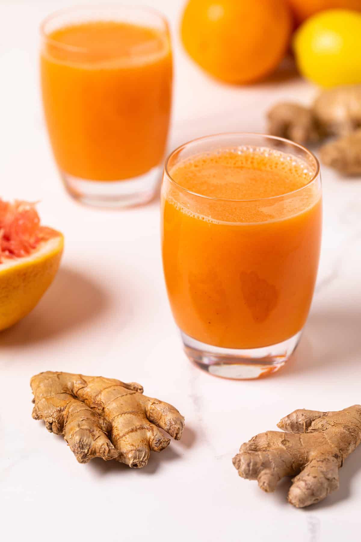 Carrot Ginger Citrus Turmeric Juice in a glass with fresh ginger root.