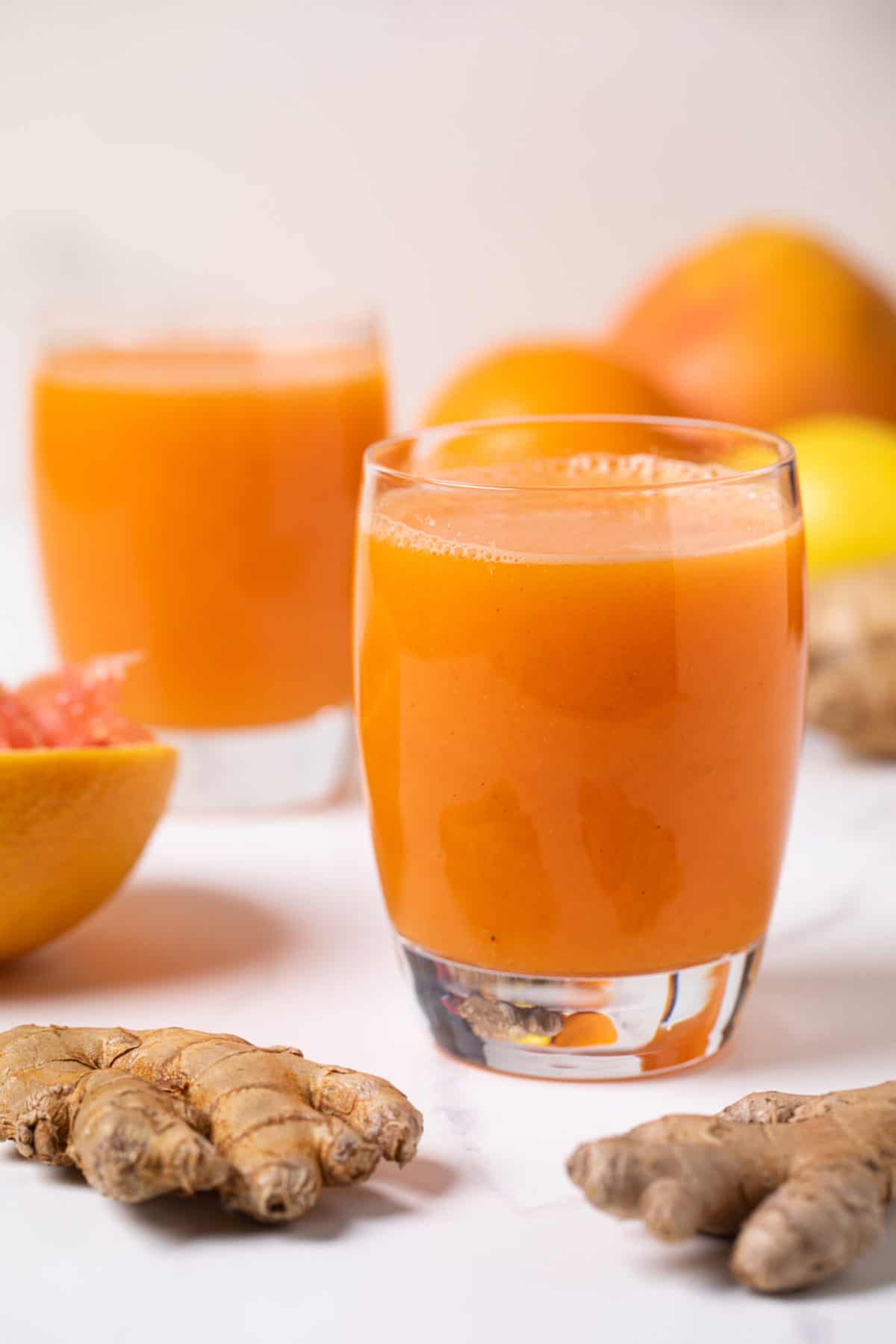 Carrot Ginger Citrus Turmeric Juice in a glass with fresh ginger root and orange slices.