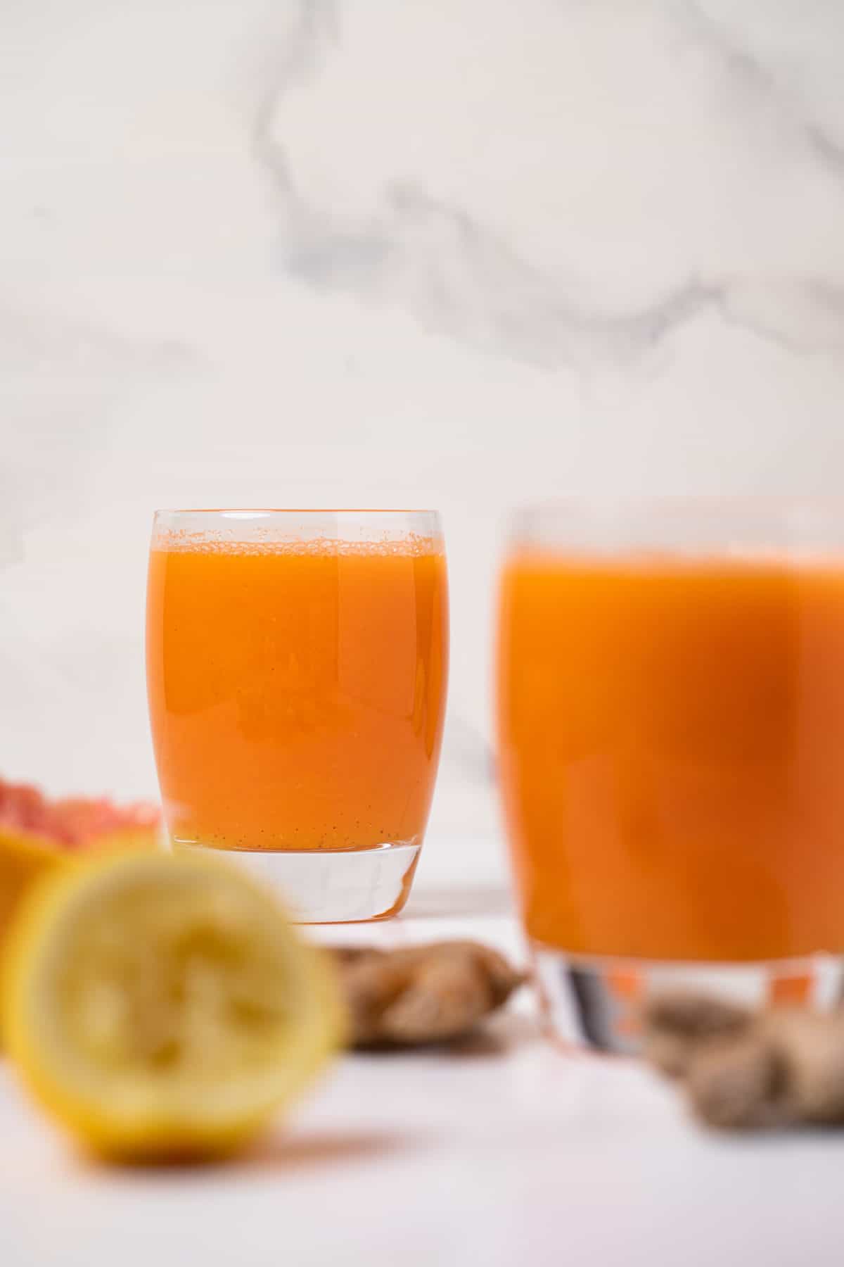 Carrot Ginger Citrus Turmeric Juice in a glass with fresh ginger root and lemon slices.