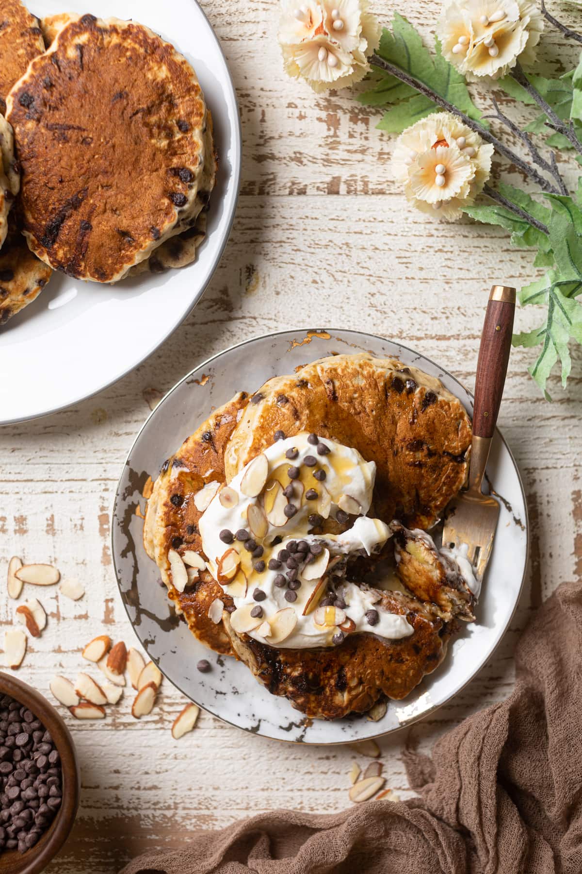 Plate of Vegan Banana Chocolate Chip Pancakes topped with coconut whipped cream, nuts, and chocolate chips