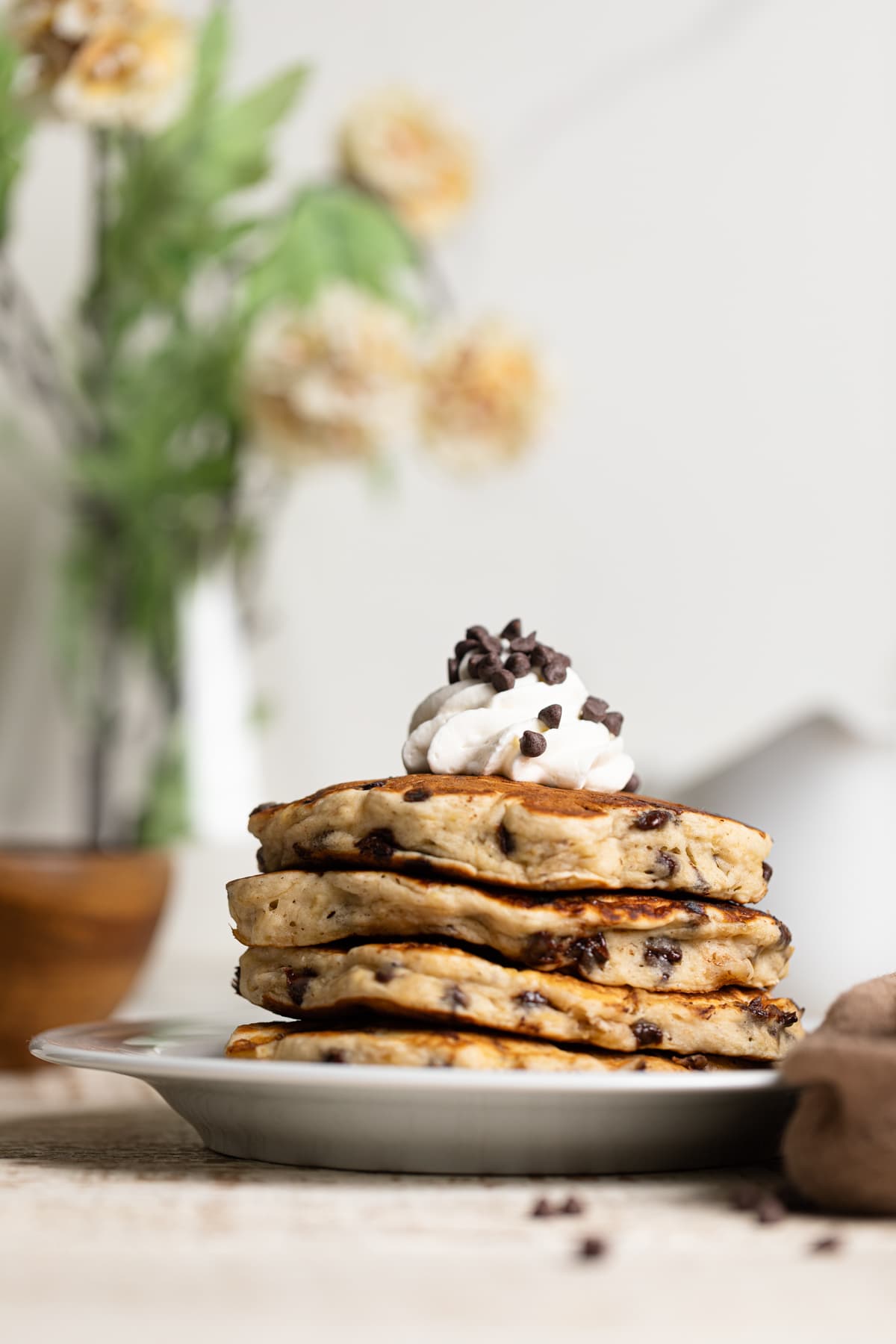 Stack of Vegan Banana Chocolate Chip Pancakes topped with coconut whipped cream and chocolate chips