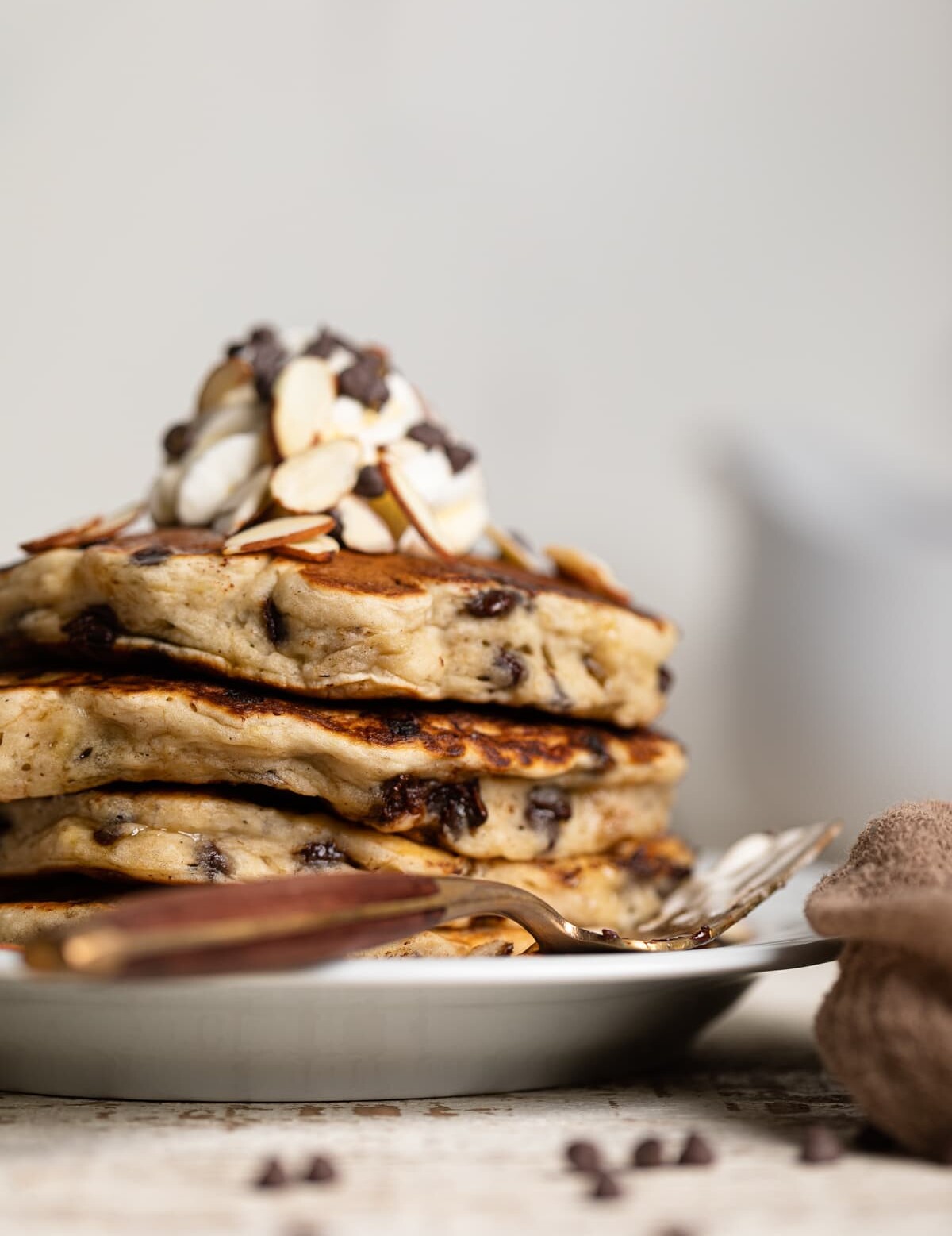 Stack of Vegan Banana Chocolate Chip Pancakes topped with nuts, coconut whipped cream, and chocolate chips