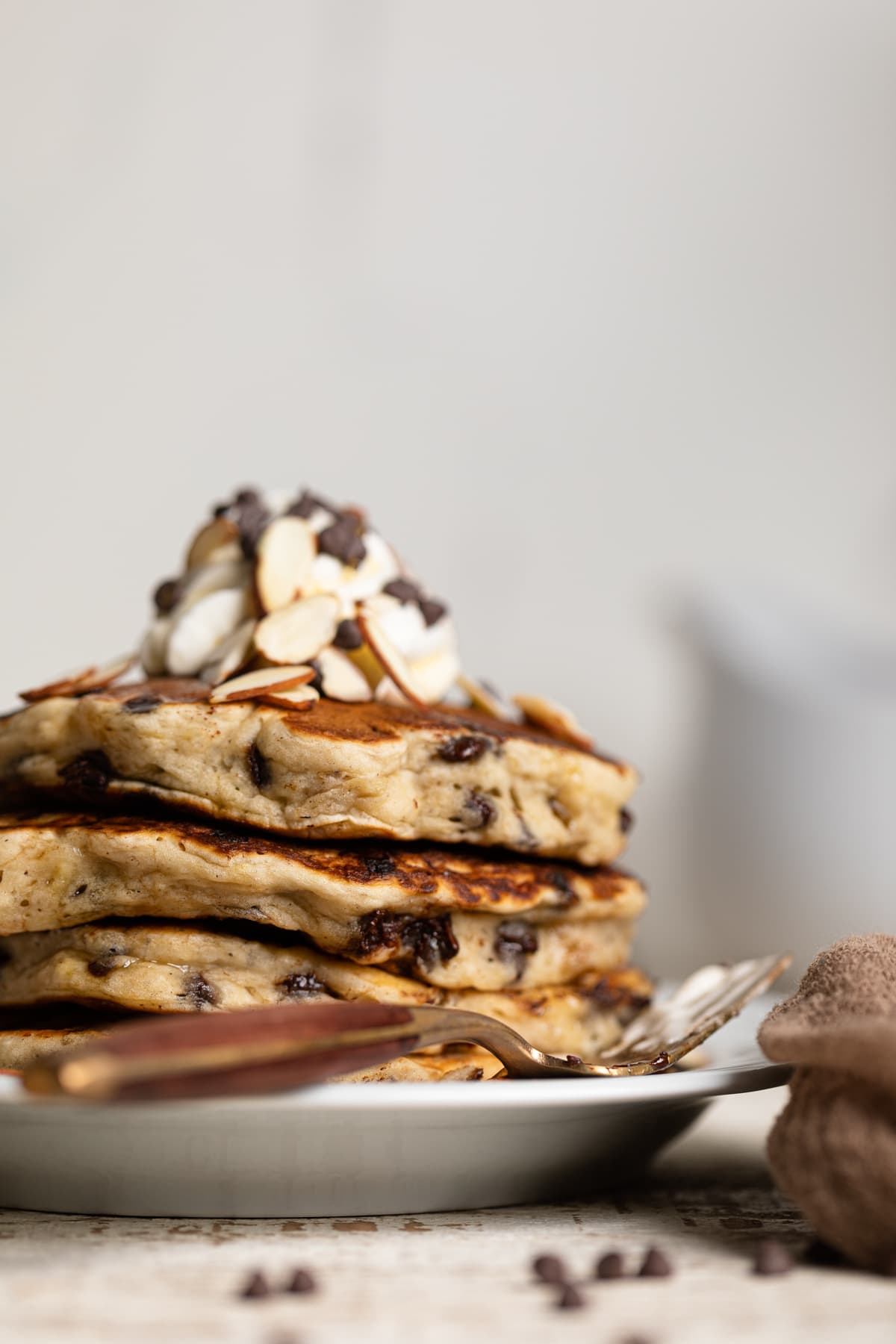 Stack of Vegan Banana Chocolate Chip Pancakes topped with nuts, coconut whipped cream, and chocolate chips