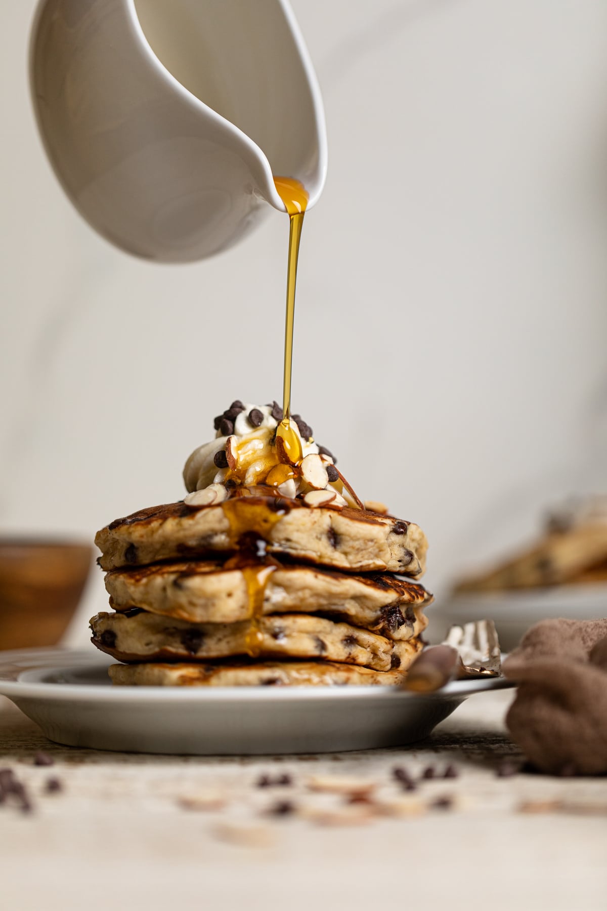 Syrup pouring on a stack of Fluffy Vegan Banana Chocolate Chip Pancakes