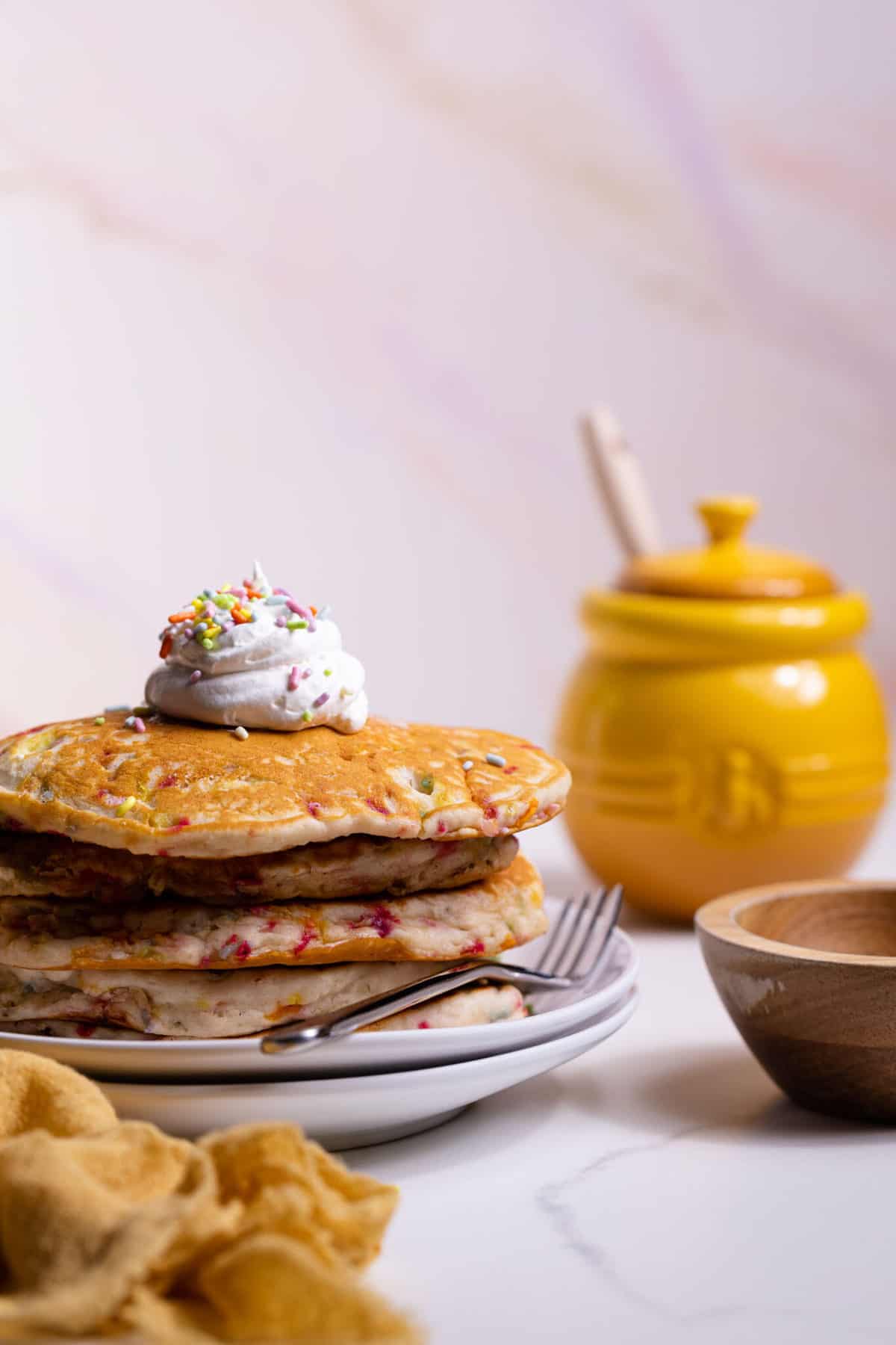 Funfetti Vegan Pancakes in a stack with whipped cream on top and a fork.