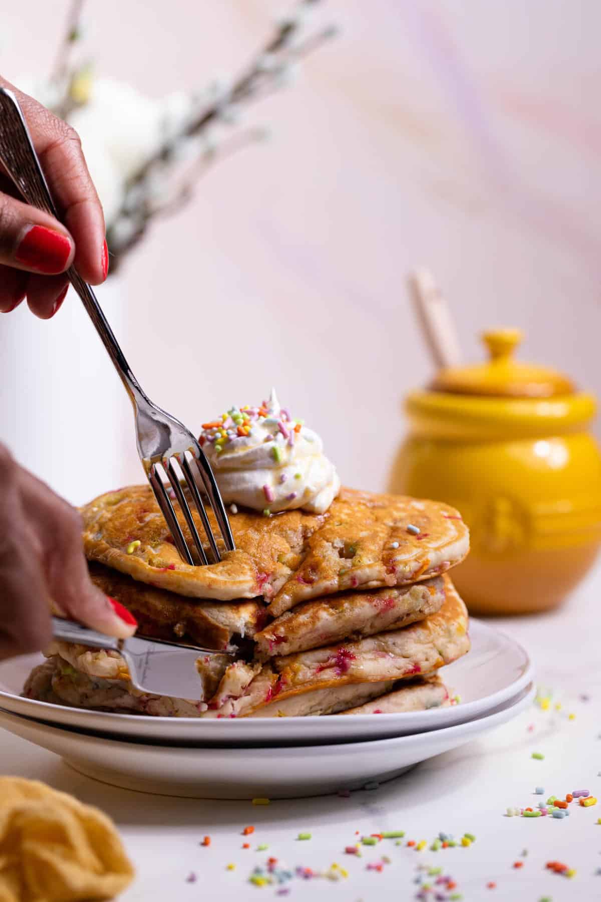 Funfetti Vegan Pancakes in a stack with whipped cream on top and a fork and knife taking a bite.