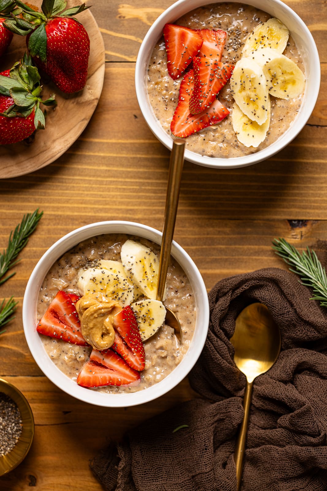 Two bowls of oatmeal with fruits and a spoon.