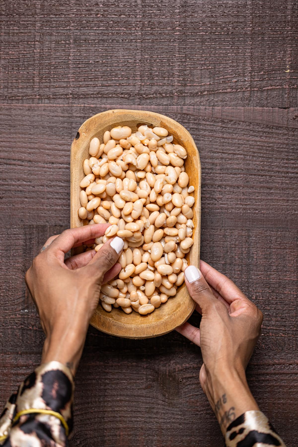 Hand grabbing some white beans out of a wooden bowl