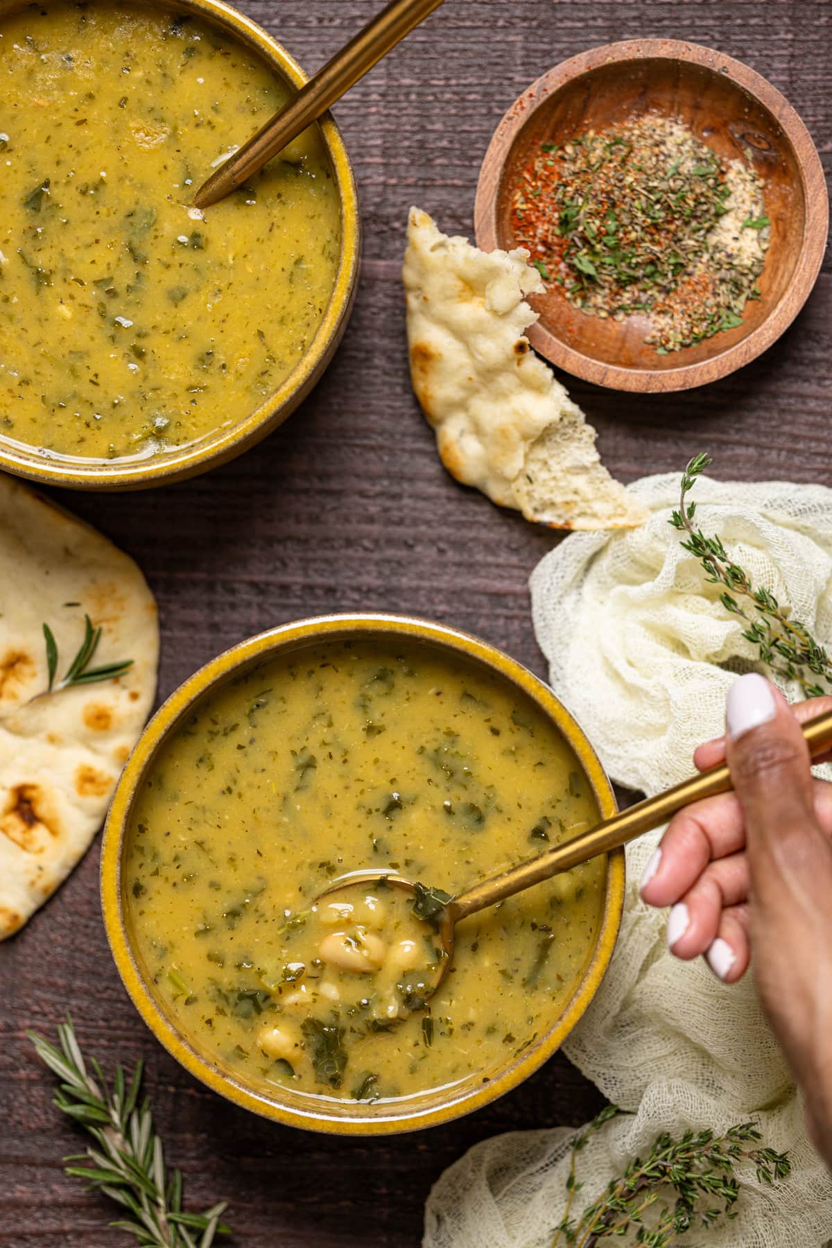 Overhead shot of a hand dipping a spoon into a bowl of Creamy Vegan White Bean Soup 