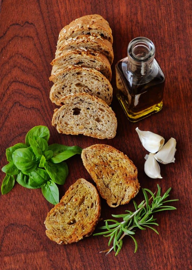 Slices of bread on a wooden surface with garlic, oil, and herbs.