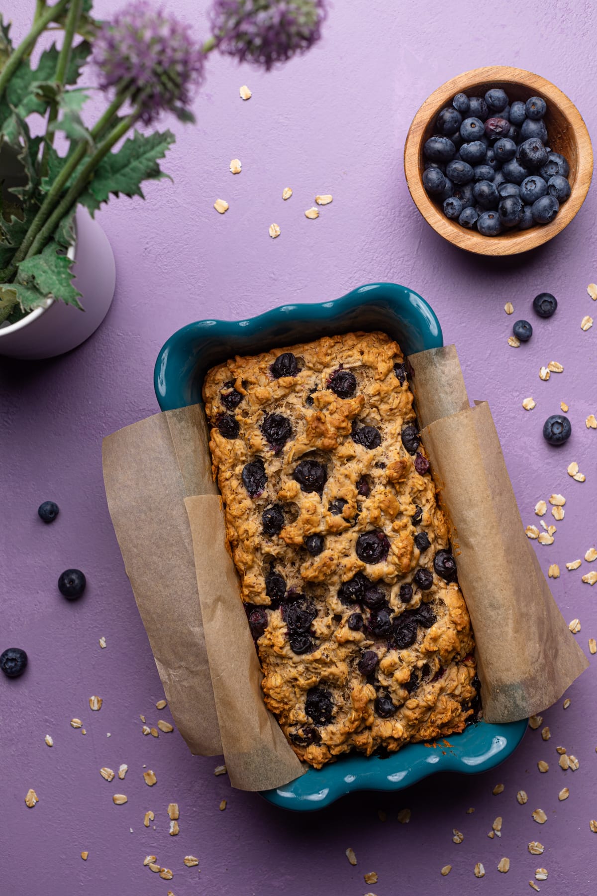 Blueberry Oatmeal Breakfast Bread in a loaf pan with fresh flowers.