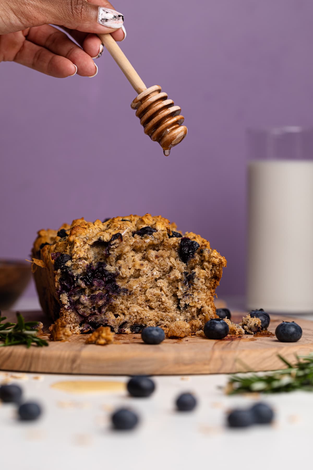 Blueberry Oatmeal Breakfast Bread loaf with honey being drizzled on top.