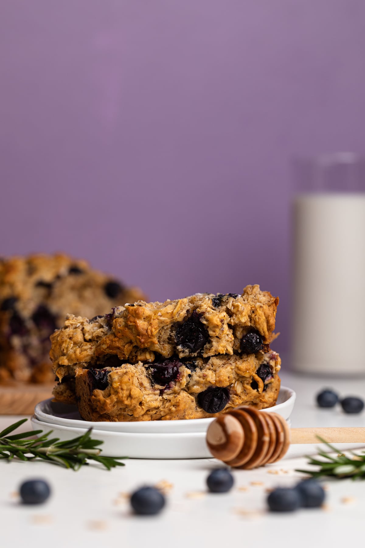 Blueberry Oatmeal Breakfast Bread slices on a plate with fresh berries and rosemary.