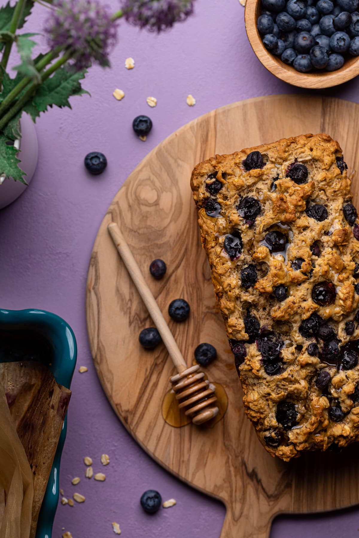 Blueberry Oatmeal Breakfast Bread on a wooden cutting board with a honey dipper.