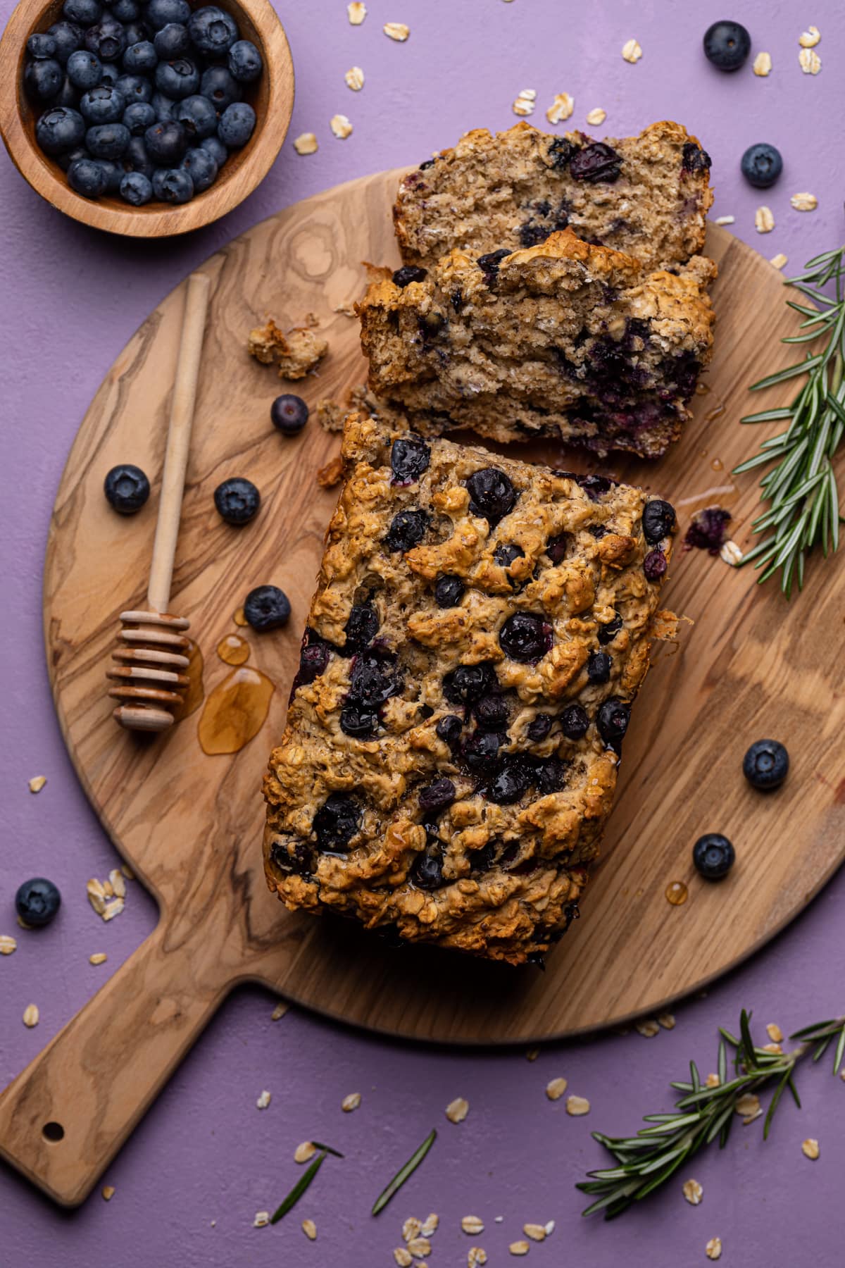 Blueberry Oatmeal Breakfast Bread on a cutting board with a honey stirrer.