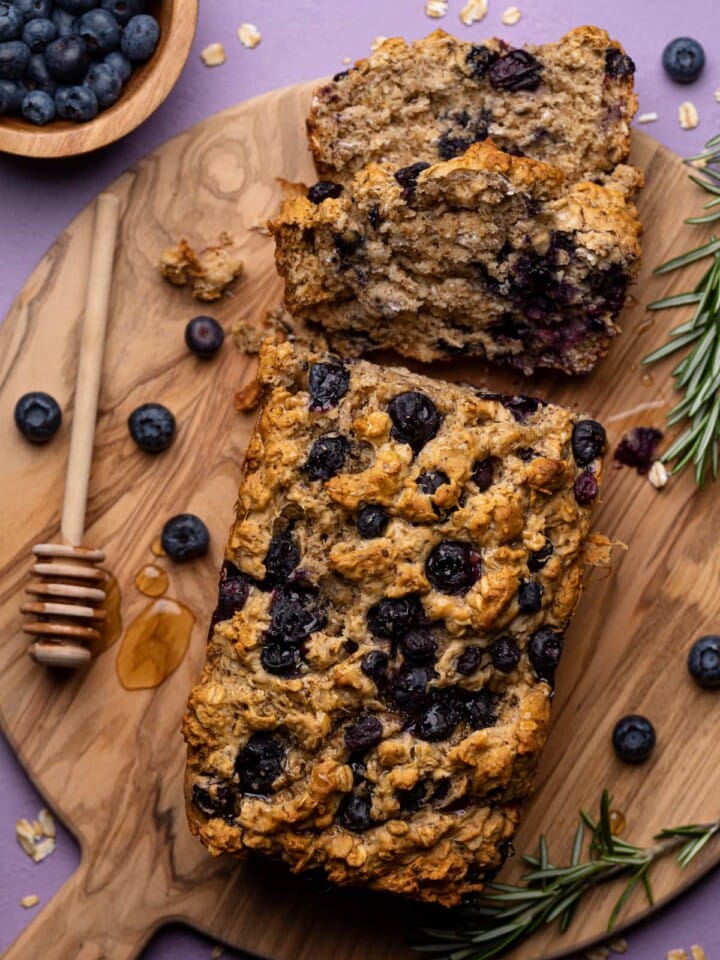 Partially sliced loaf of Blueberry Oatmeal Breakfast Bread on a wooden board.