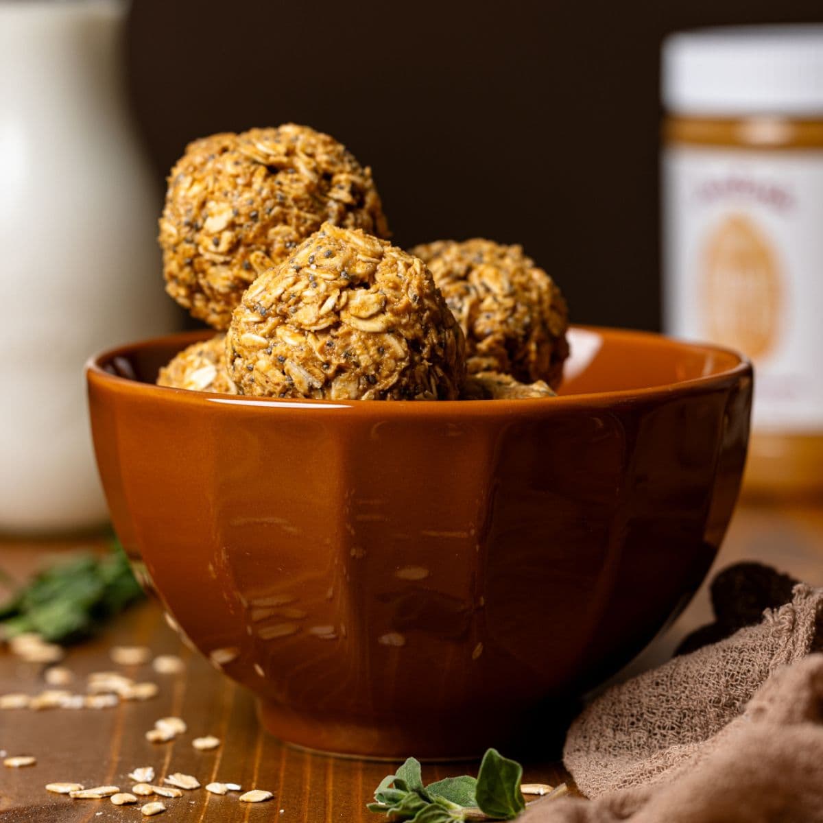 Energy balls in a brown bowl with a glass of milk and jar of peanut butter.