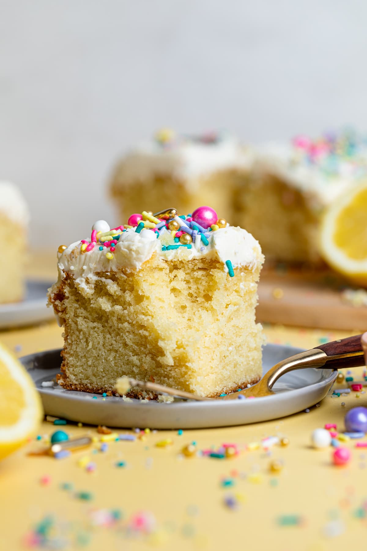 Slice of cake on a white plate with fork and lemons and sprinkles.