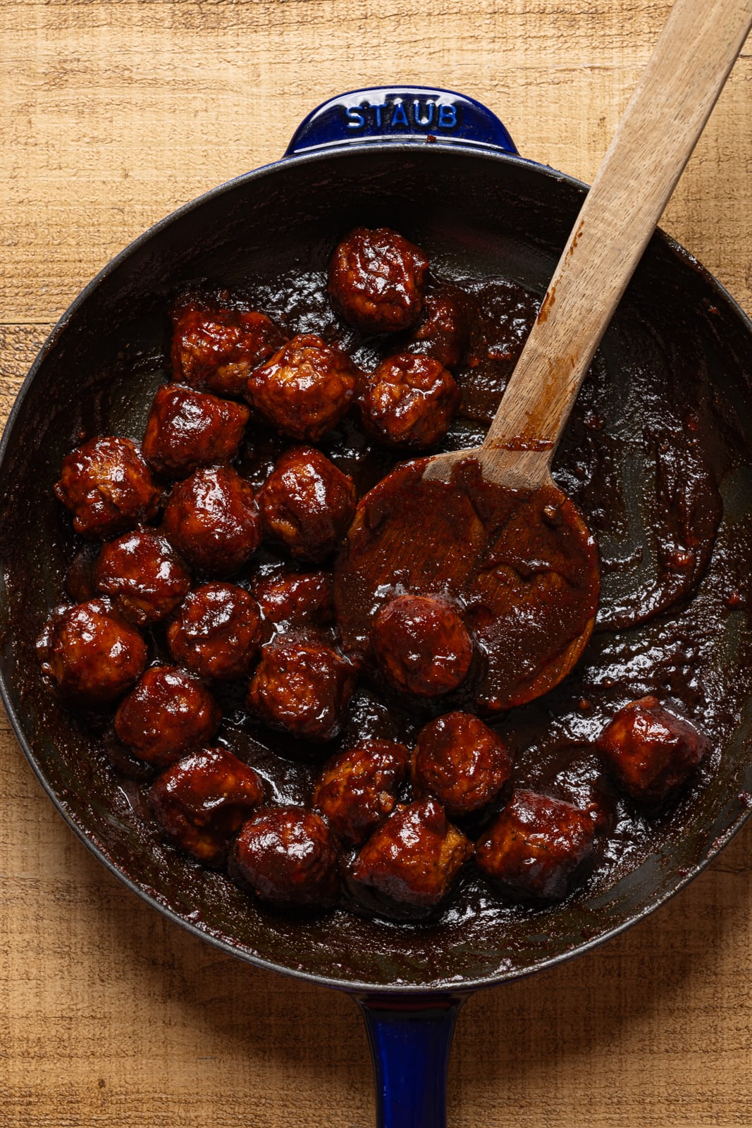 BBQ meatballs in a skillet with a wooden spoon.