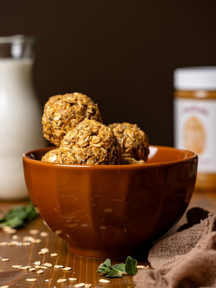 Energy balls in a brown bowl with a glass of milk and jar of peanut butter.