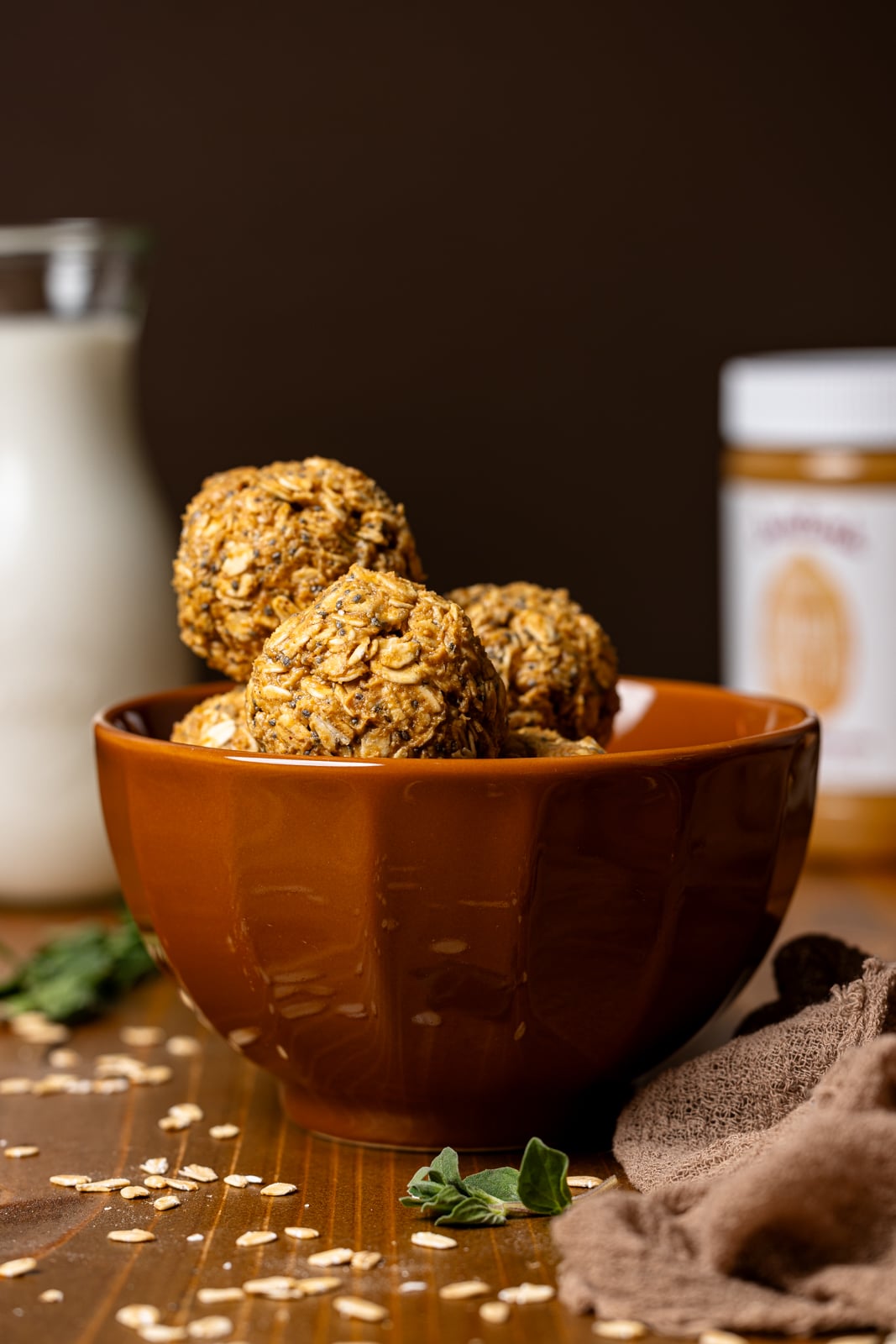 Energy balls in a brown bowl with a glass of milk and jar of peanut butter.
