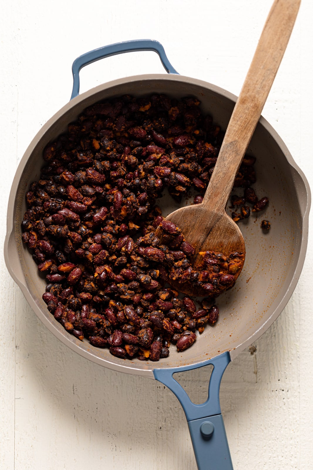 Wooden spoon stirring seasoned beans in a pan