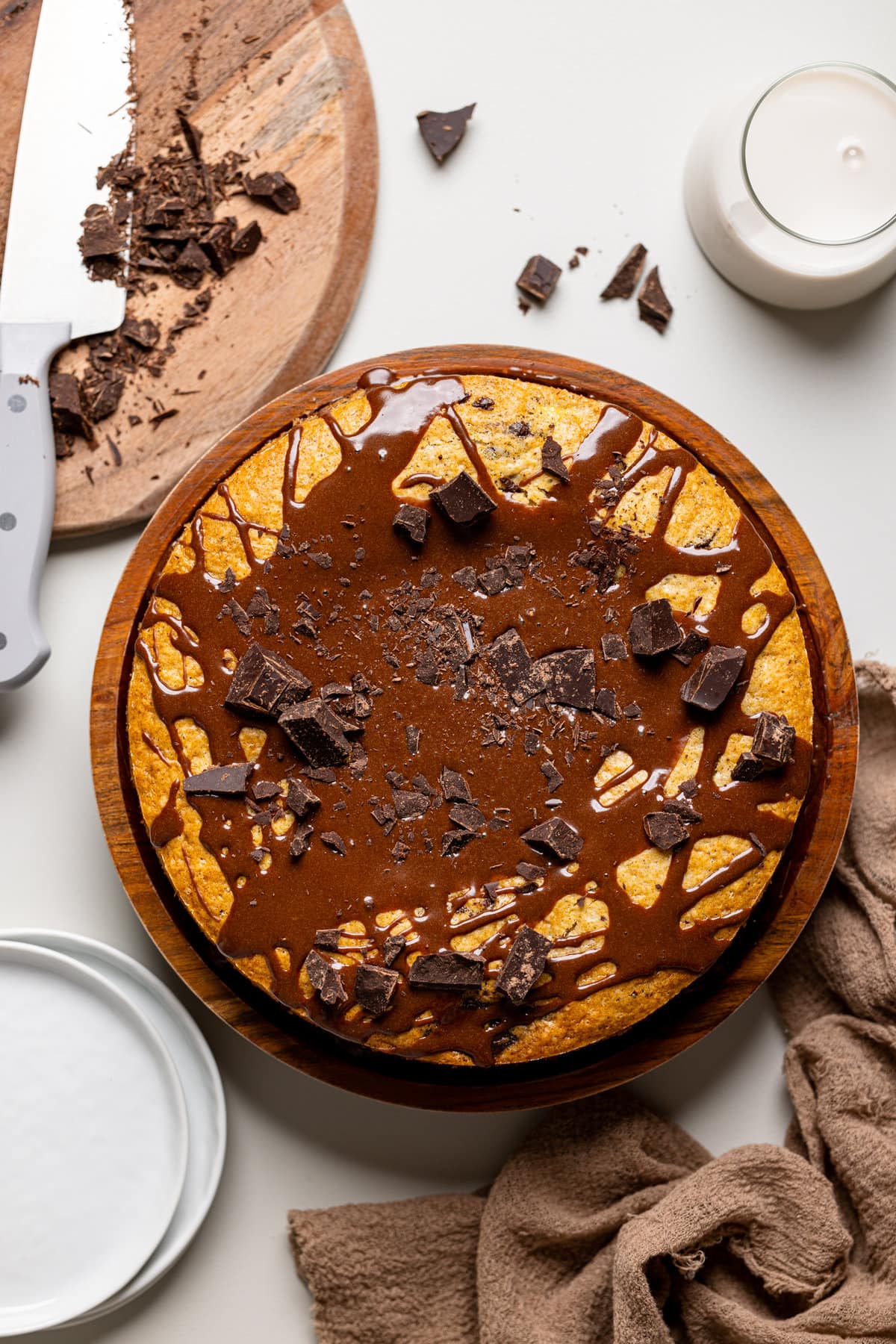 Chocolate banana cake atop a brown wood cake stand with a chocolate drizzle and chopped chocolate.