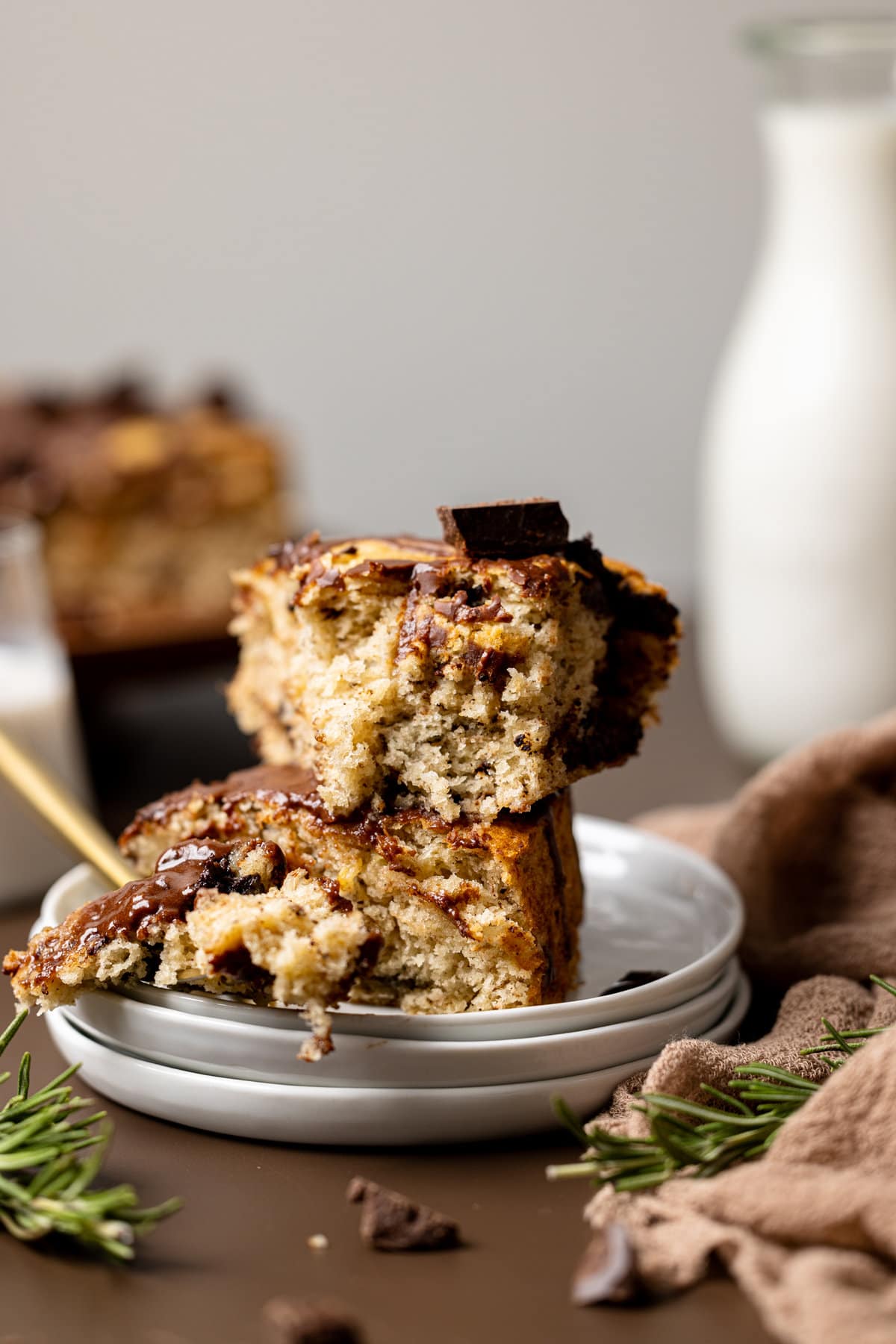 Two slices of banana cake stacked atop each other on a white plate on a brown table and with a fork.