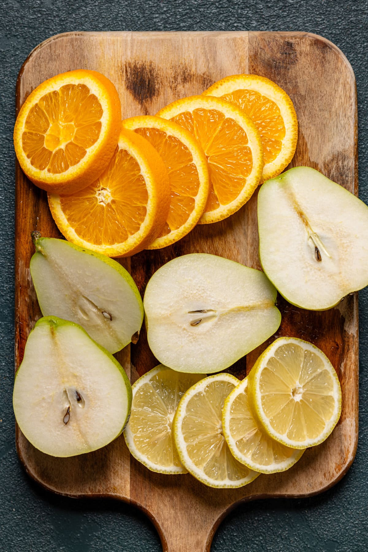 Sliced oranges, lemon, and pears on a cutting board.