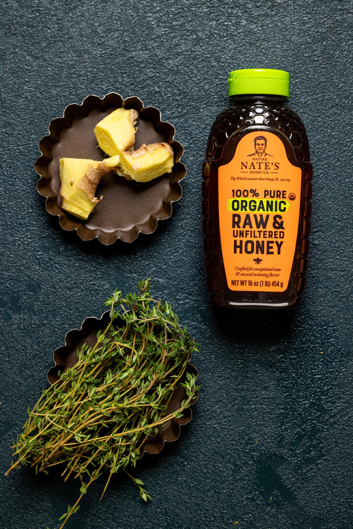 Chopped ginger, honey, and thyme sprigs on a dark green table.