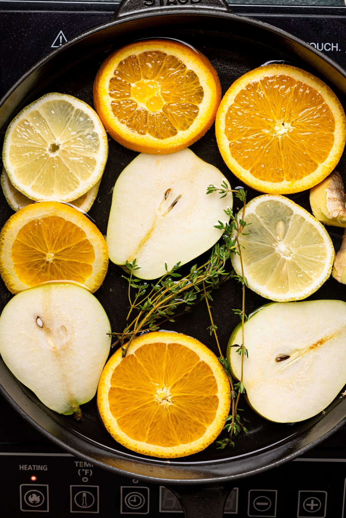 Slices of citrus, pears, and thyme sprigs in a pot of water.