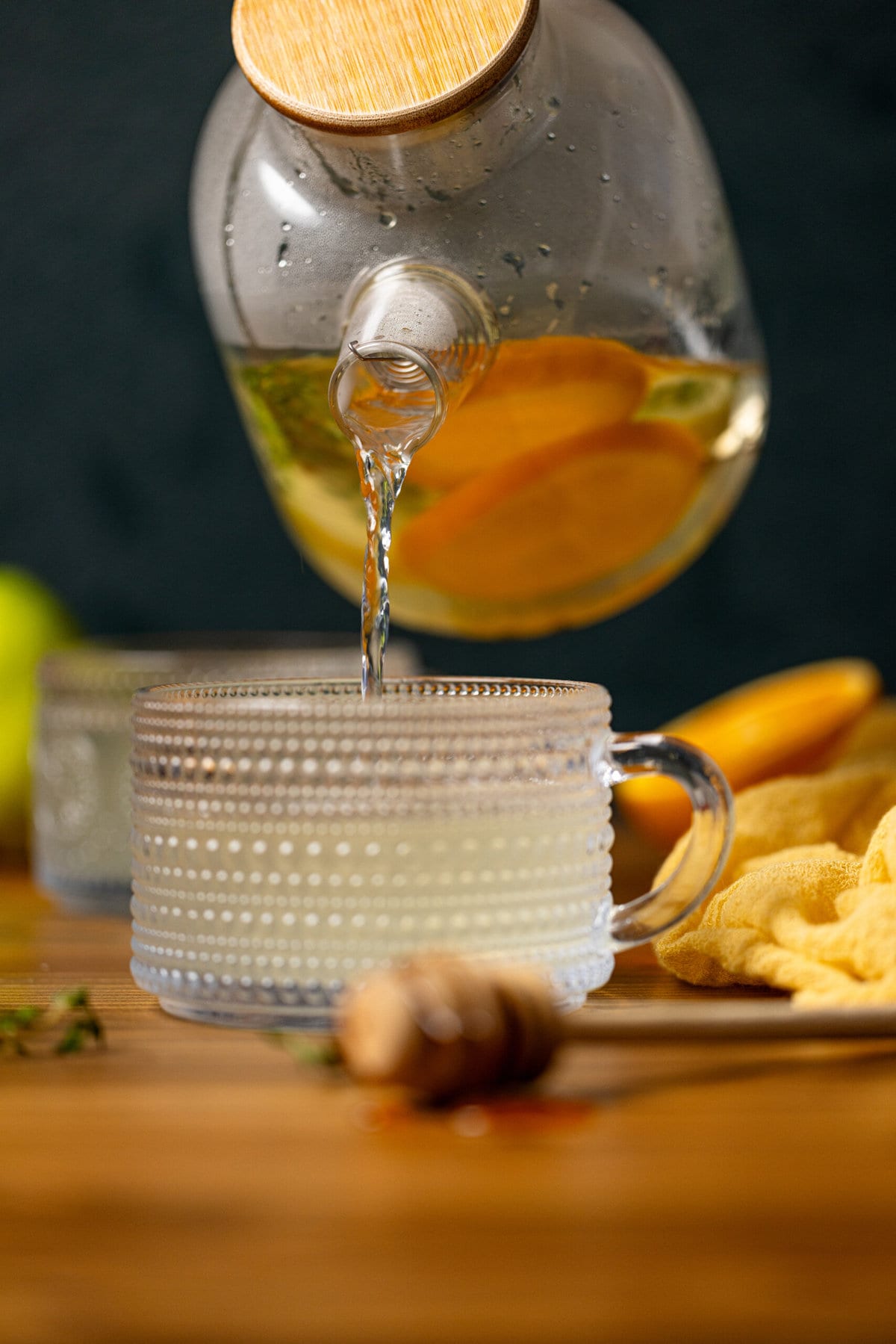 Healthy Detox tea being poured into a mug with a honey stick and citrus around.